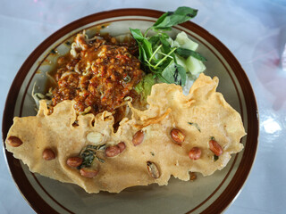 This is Pecel, a traditional Javanese dish made of mixed steamed vegetables topped with spicy peanut sauce, served with a crispy peanut cracker (rempeyek) and fresh herbs
