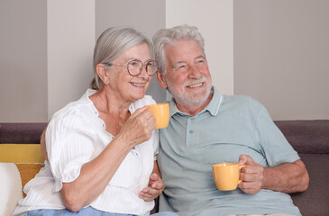 Carefree relaxed senior couple sitting on sofa with a coffee cup, recollecting good memories or planning common future, enjoying peaceful moment together at home.