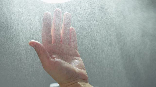 Wellness technician sprays hydrating mist onto hands under bright clinical light, creating fine droplets that shimmer before facial treatment in tranquil spa environment for hygienic skin prep