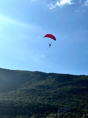 Man with a red parachute, paraplane in the air. Bright, clear sky, Green mountains in the background. Picturesque beach. Space, nature concept, retreat, sport, hobby, recreation