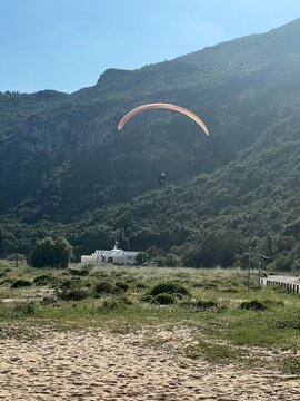 Man with a paraplane in the air. Bright, clear sky, Green mountains in the background. Picturesque beach. Space, nature concept, retreat, sport, hobby, recreation