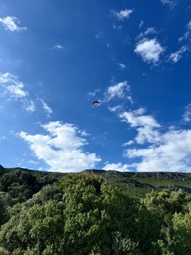 Man with a red parachute, paraplane in the air. Bright, clear sky, Green mountains in the background. Picturesque beach. Space, nature concept, retreat, sport, hobby, recreation