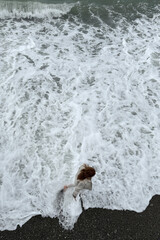 Girl walking along the seashore in stormy waves. Top view