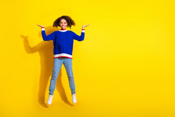 Smiling young woman jumping and posing in casual colorful attire against a vibrant yellow background