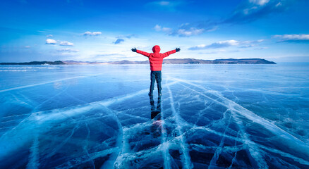 Traveler man wear red clothes and raising arm standing on natural breaking ice in frozen water at Lake Baikal, Siberia, Russia.