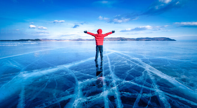 Fototapeta Traveler man wear red clothes and raising arm standing on natural breaking ice in frozen water at Lake Baikal, Siberia, Russia.