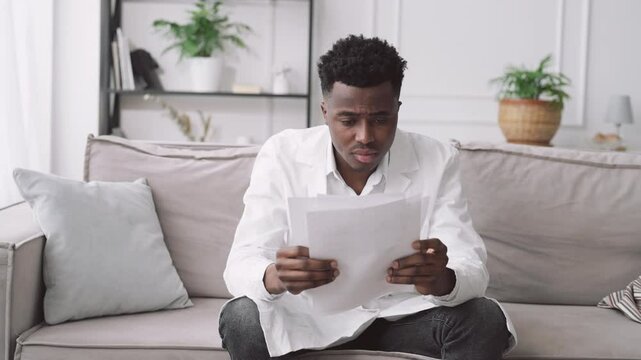 Portrait of virologist viewing medical records and feeling tiredness, black man. Medical student sitting alone in clinic office, intern studying in modern hospital, health professional working