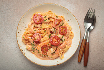 Seafood linguine pasta in creamy sauce with shrimp and cherry tomatoes, garnished with fresh parsley, served on a light warm beige background with cutlery top view