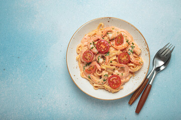 Seafood linguine pasta in creamy sauce with shrimp and cherry tomatoes, garnished with fresh parsley, served on a light blue background with cutlery top view, copy space