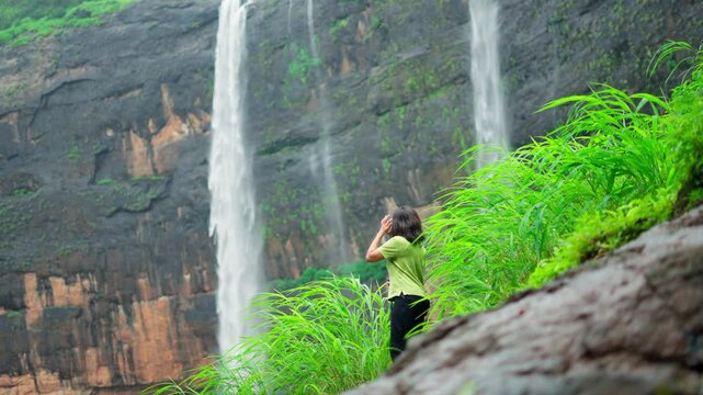 4K shot of Hiker girl standing looking at Kataldhar waterfall at Lonavala, Maharashtra, India. Tourist exploring Sahyadri mountains during monsoon season. Scenic view of waterfall.