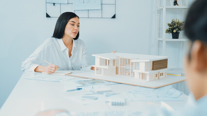 Professional asian male project manager hand puts the map on meeting table while discuss and brainstorm with coworker about building project at meeting room with blueprint hand behind. Immaculate.