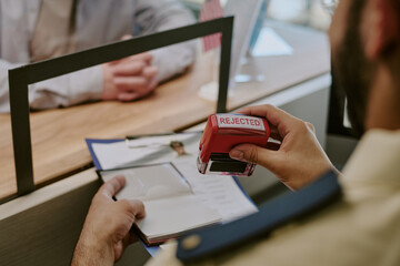 Hands stamping documents with rejected stamp at desk while communicating with another person with focused and intent expression