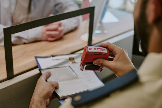 Hands stamping documents with rejected stamp at desk while communicating with another person with focused and intent expression