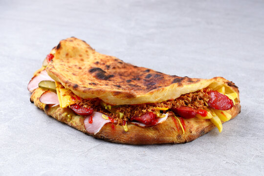 Folded Pizza Sandwich Panuozzo with Ham, Sausage, Cheese and Pickles on Stone Surface