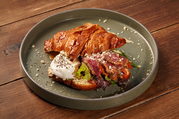 Delicious croissant sandwich with roast beef and poached egg on wooden table