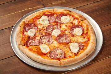 Delicious pizza with salami, cream cheese and grated cheese resting on wooden table