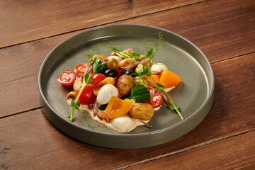 Delicious mediterranean salad with potatoes, cherry tomatoes, cucumber, olives, eggs, and orange pepper on rustic wooden table