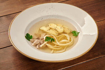Chicken consomme soup with egg noodles and parsley in white bowl on rustic wooden table