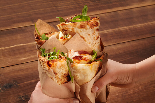 Hands holding pizza wraps with arugula on rustic wooden table