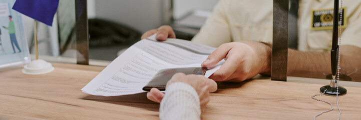 Plakat Person handing over document across counter in busy visa office with hands visible on both sides adding sense of interaction and engagement