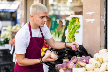 Grocery store employee places ripe radish on a display case at a street store