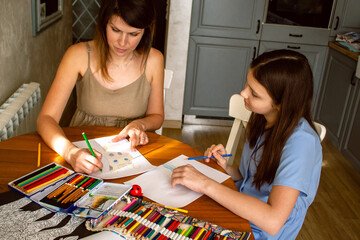 Mother teaching daughter to draw sitting in home kitchen. Cozy candid shot of family love. For...
