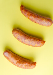 Three raw smoked sausages on yellow background in studio light for food packaging, advertisement, and culinary design use