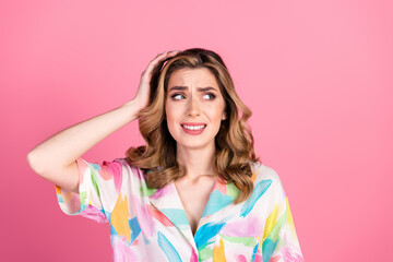 Young woman with a confused facial expression posing against a pink background in a colorful shirt
