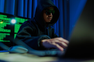 Male hacker in a dark room trying to steal global user data to sell on the dark web, representing serious threats in modern cybercrime.