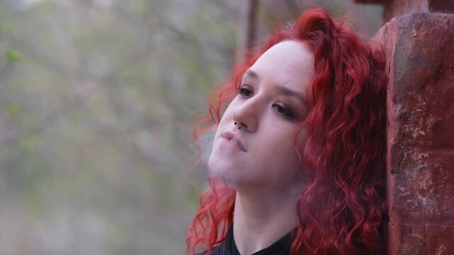 Teen Vaper. Young girl with curly hair smokes an electronic cigarette against a brick wall on the street. Bad habit.