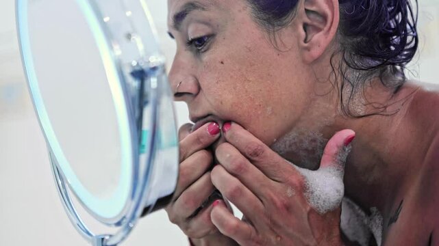 Woman squeezing pimples in her face in mirror during bath
