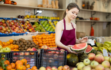 Female salesman in an apron carefully places ripe watermelons on a supermarket counter