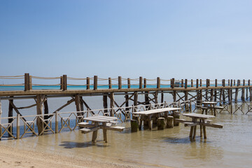 Wooden pier over shallow water with submerged picnic tables on a sandy beach, highlighting unique resort dining concept for summer vacation destination.