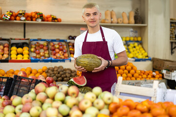 Male salesman in an apron carefully places ripe watermelons on a supermarket counter