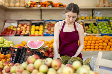 Female seller received a shipment of ripe red watermelons and lays them out on the counter in a supermarket