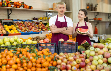 Man and a woman sellers are standing near a fruit counter in a supermarket. Grocery store workers offer farm-fresh fruits and vegetables