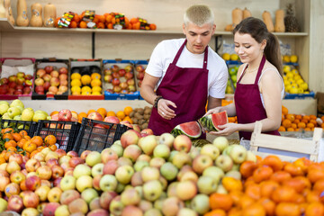 Male seller helps a female seller puts fresh watermelons on the counter. Sellers have received a delivery of fruit and are putting them on display