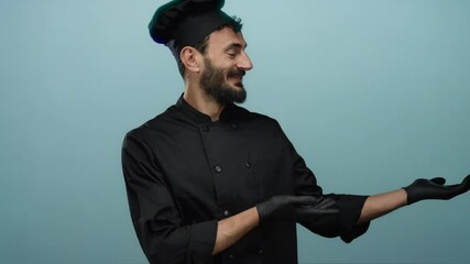 Hispanic chef in black uniform and gloves presenting with open hands against a blue background, smiling confidently in a culinary context.