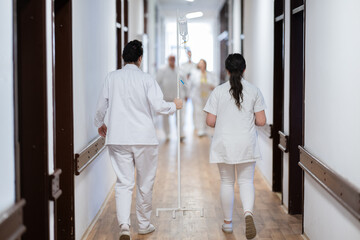 A group of healthcare professionals in white uniforms walking through a hospital hallway while reviewing patient documents and discussing treatment plans.