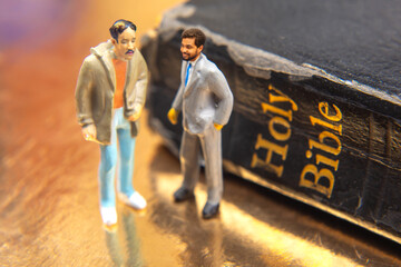 Two miniature figurines, one in a suit and one in casual attire, standing on a golden surface...