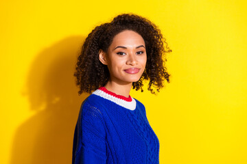 Young woman in a blue sweater smiling confidently against a cheerful bright yellow background