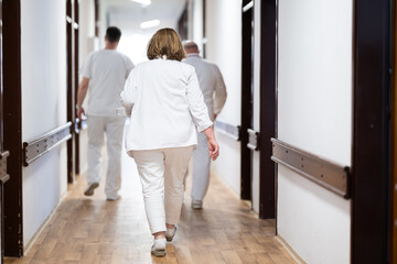 Fototapeta premium A group of healthcare professionals in white uniforms walking through a hospital hallway while reviewing patient documents and discussing treatment plans.