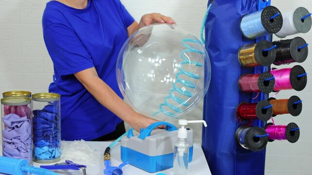 A female aerodesigner inflates a transparent balloon with white feathers with a hand pump.