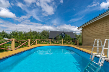 An outdoor private swimming pool surrounded by lush greenery against a blue sky on a sunny summer day.