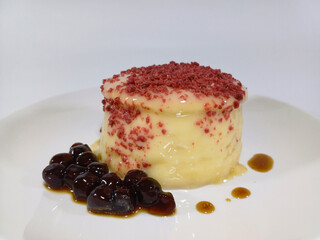 A single, delicate souffle pancake, characterized by its light and airy texture, is presented on a white plate. The pale yellow pancake is topped with a sprinkling of vibrant red crumbs and a drizzle