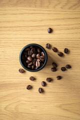 Top view of roasted coffee beans in a round coffee grinder. The beans are scattered on the wooden table in the background.