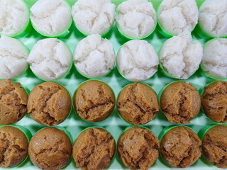 Rows of Kue Apem, small, fluffy steamed rice flour cakes, are meticulously arranged on a bright green silicone mat. The delicate Indonesian desserts come in two variations: pristine white and rich