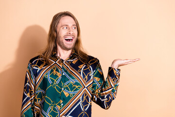 Happy young man with stylish long hair raising a hand against a beige background in a fashionable...