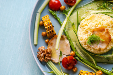 Couscous with chicken pieces, cucumbers, asparagus and corn, tomatoes and walnuts on a blue plate on a light background. Close-up.