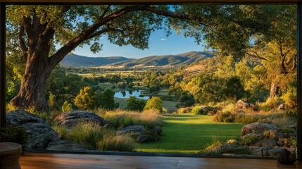   A picturesque panorama of a valley, mountains, and lake viewed from a window surrounded by lush grass and swaying trees